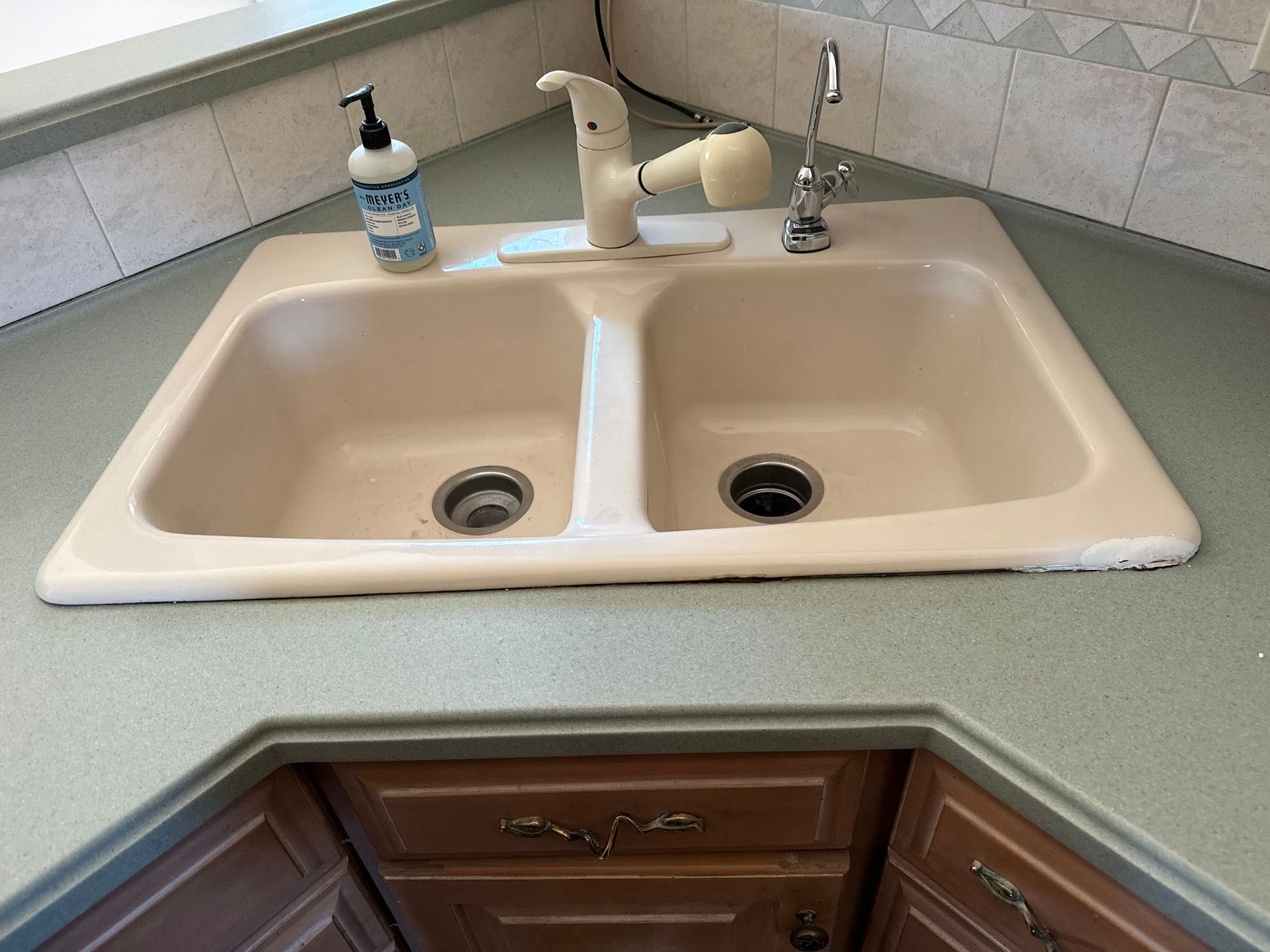 A beige double kitchen sink with a faucet, soap dispenser, and green countertops.