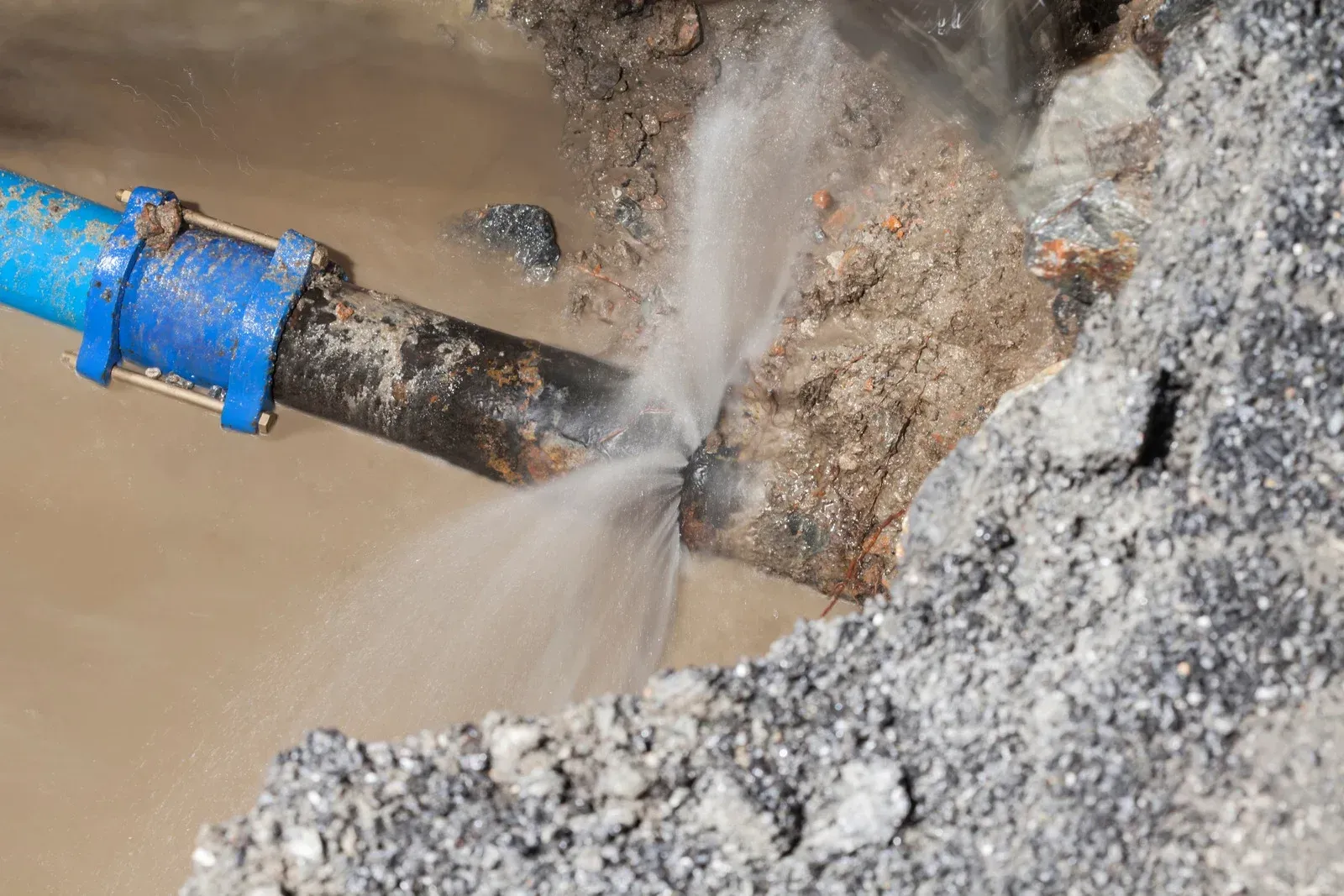 Damaged water pipe spurting water onto gravel and dirt.