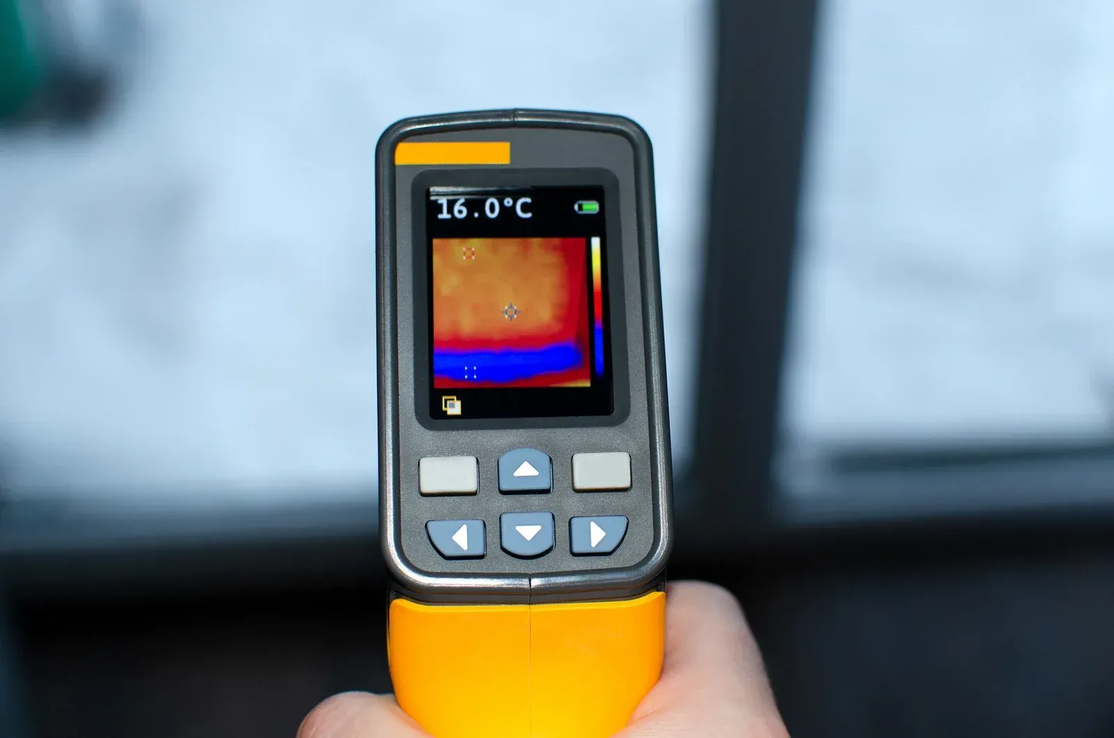 Hand holding a yellow and black thermal imaging camera, displaying a temperature of 16 degrees Celsius.