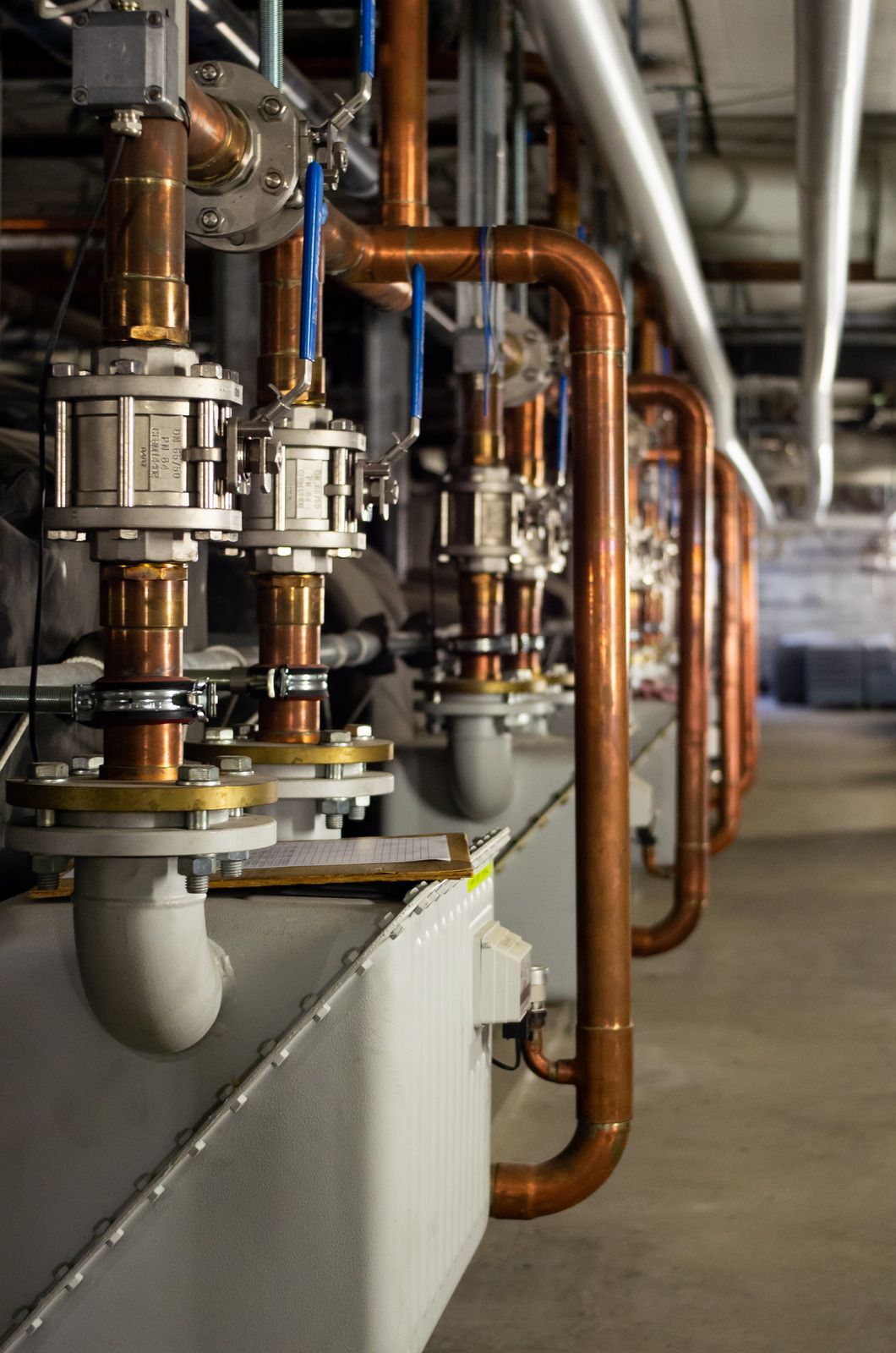 Copper pipes and valves in a mechanical room, connected to metal equipment, viewed from a low angle.