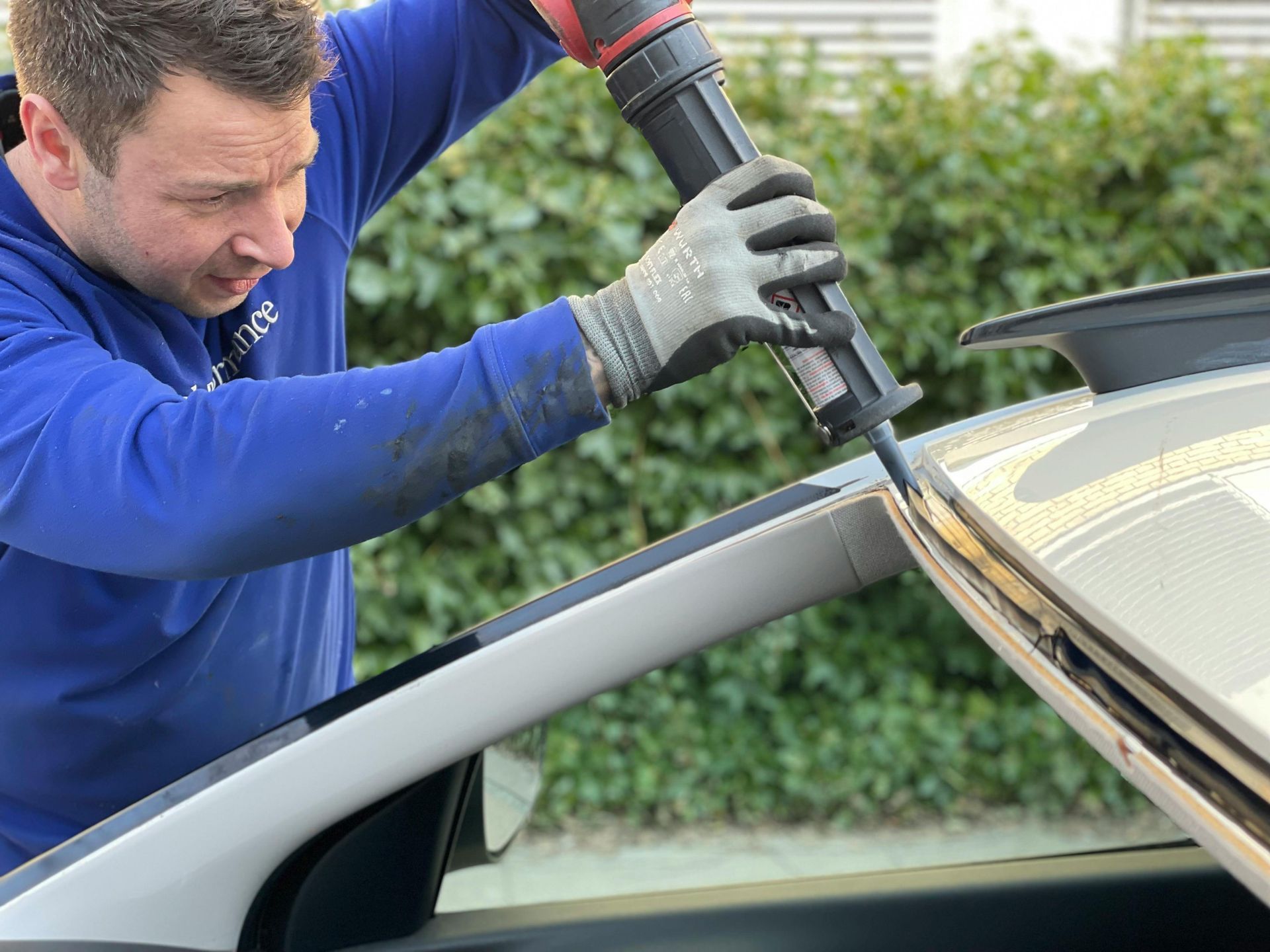Man applying sealant to a car's windshield with a caulk gun.