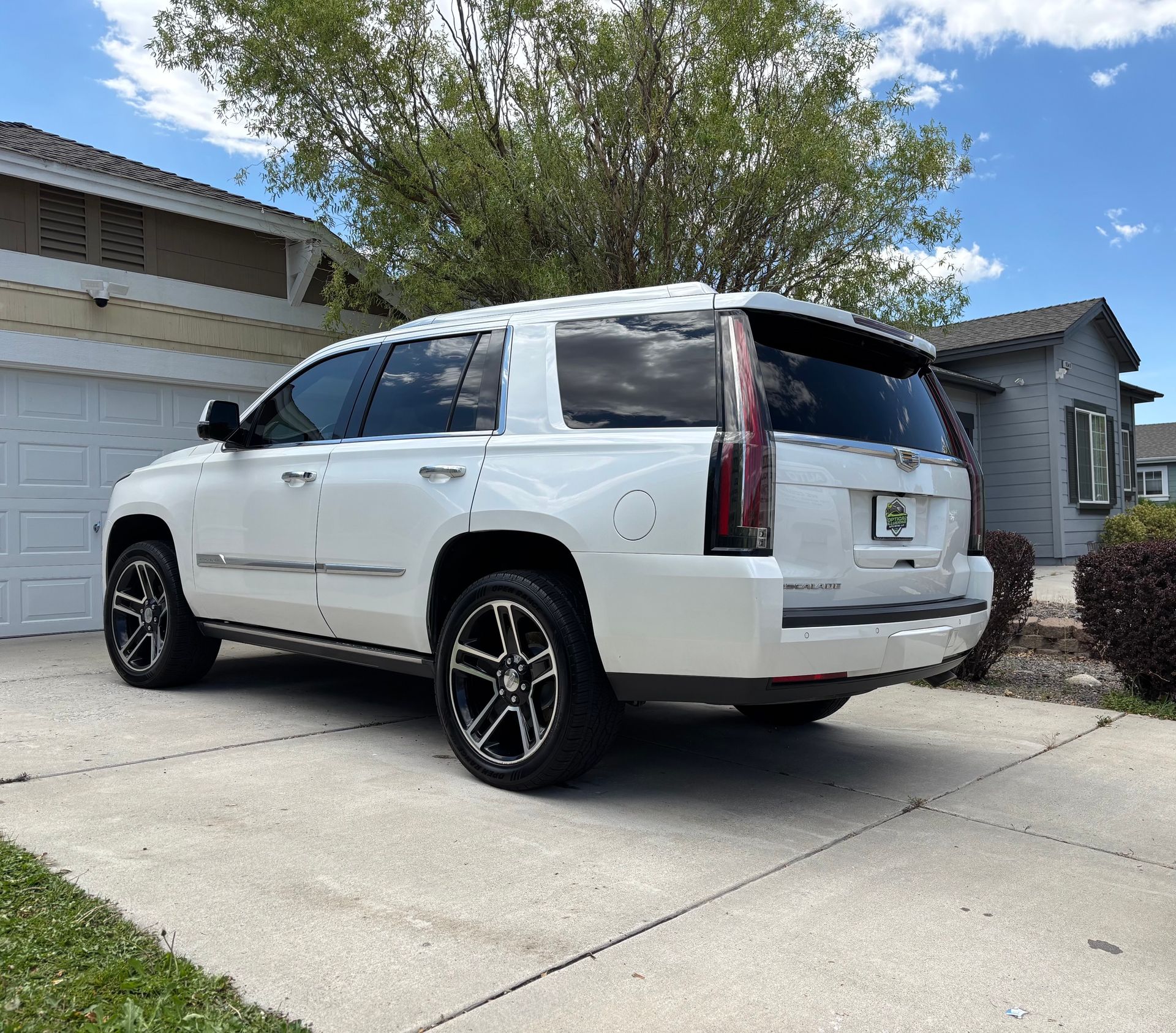 White SUV parked in a suburban driveway beside a garage, viewed from the rear side.
