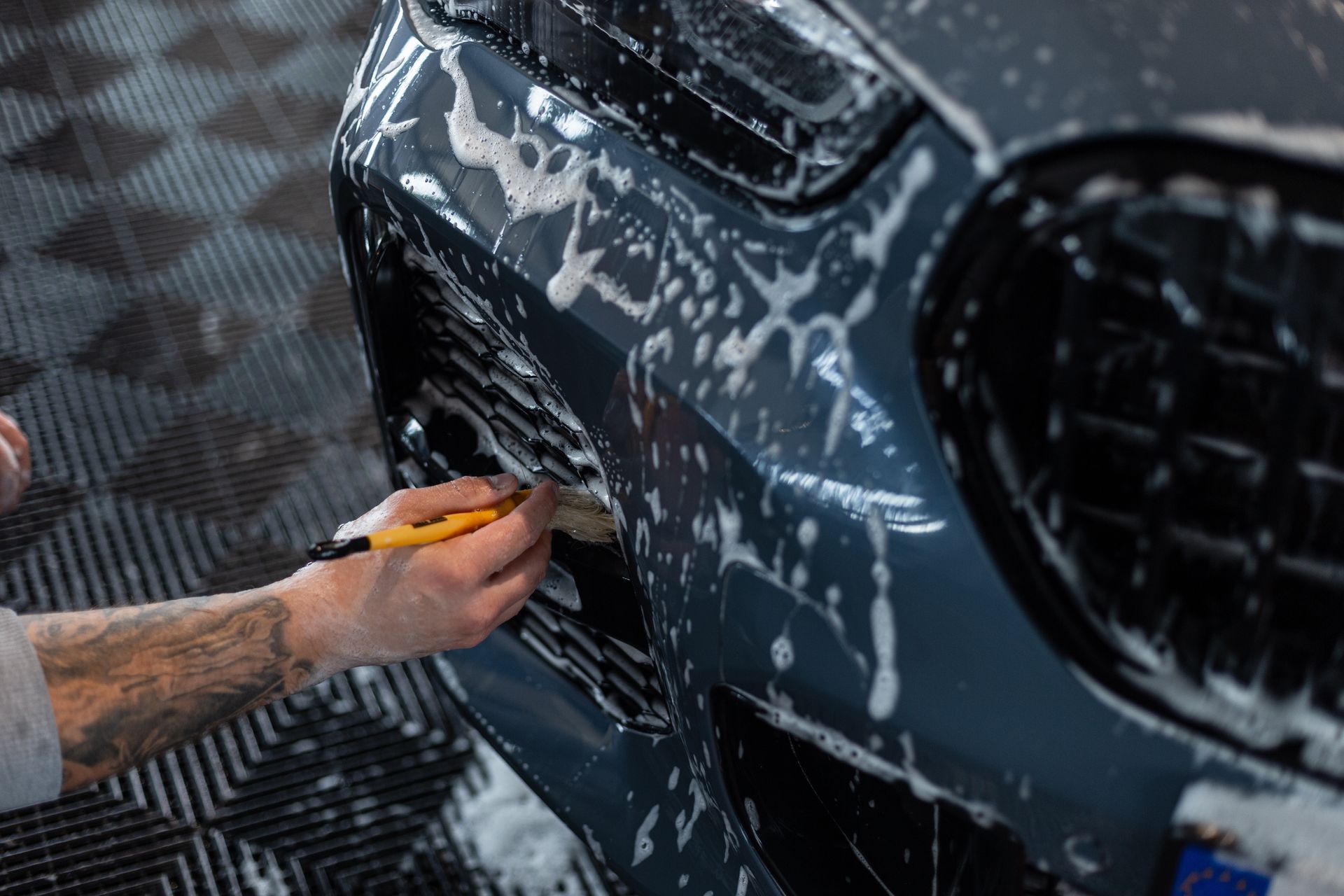 Hand using a yellow squeegee to clean soap off a dark car bumper