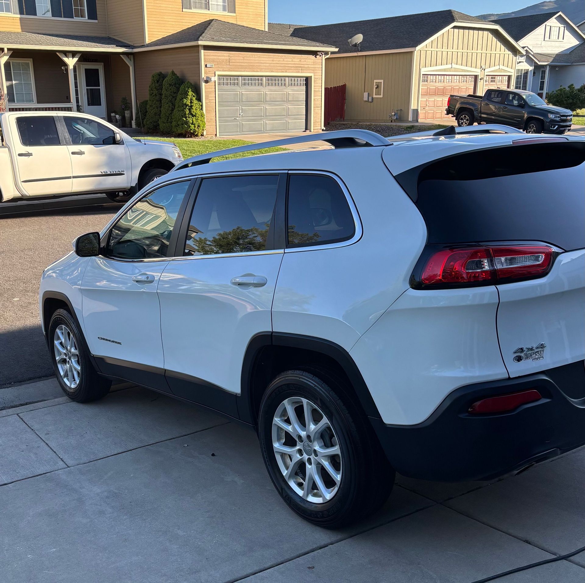 White SUV parked in a suburban driveway in front of houses, viewed from the rear side.