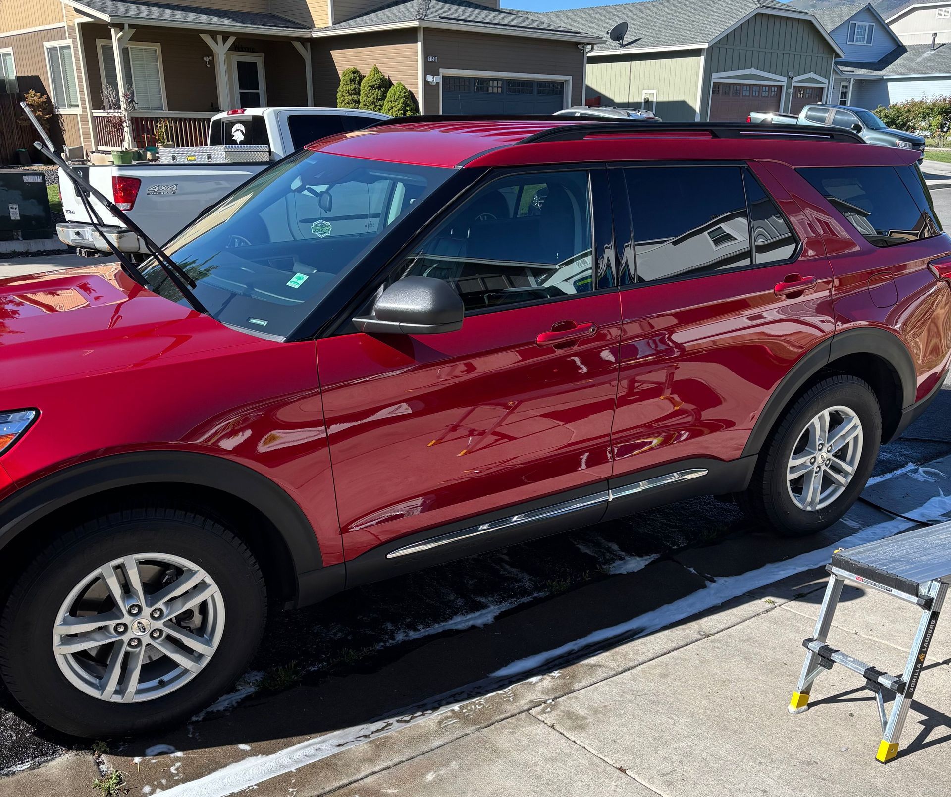 Red SUV parked in a driveway beside a house on a sunny day.