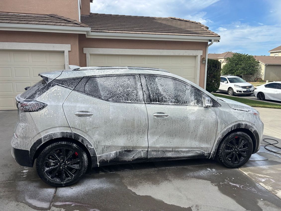 White SUV covered in foam being washed in a driveway beside a garage