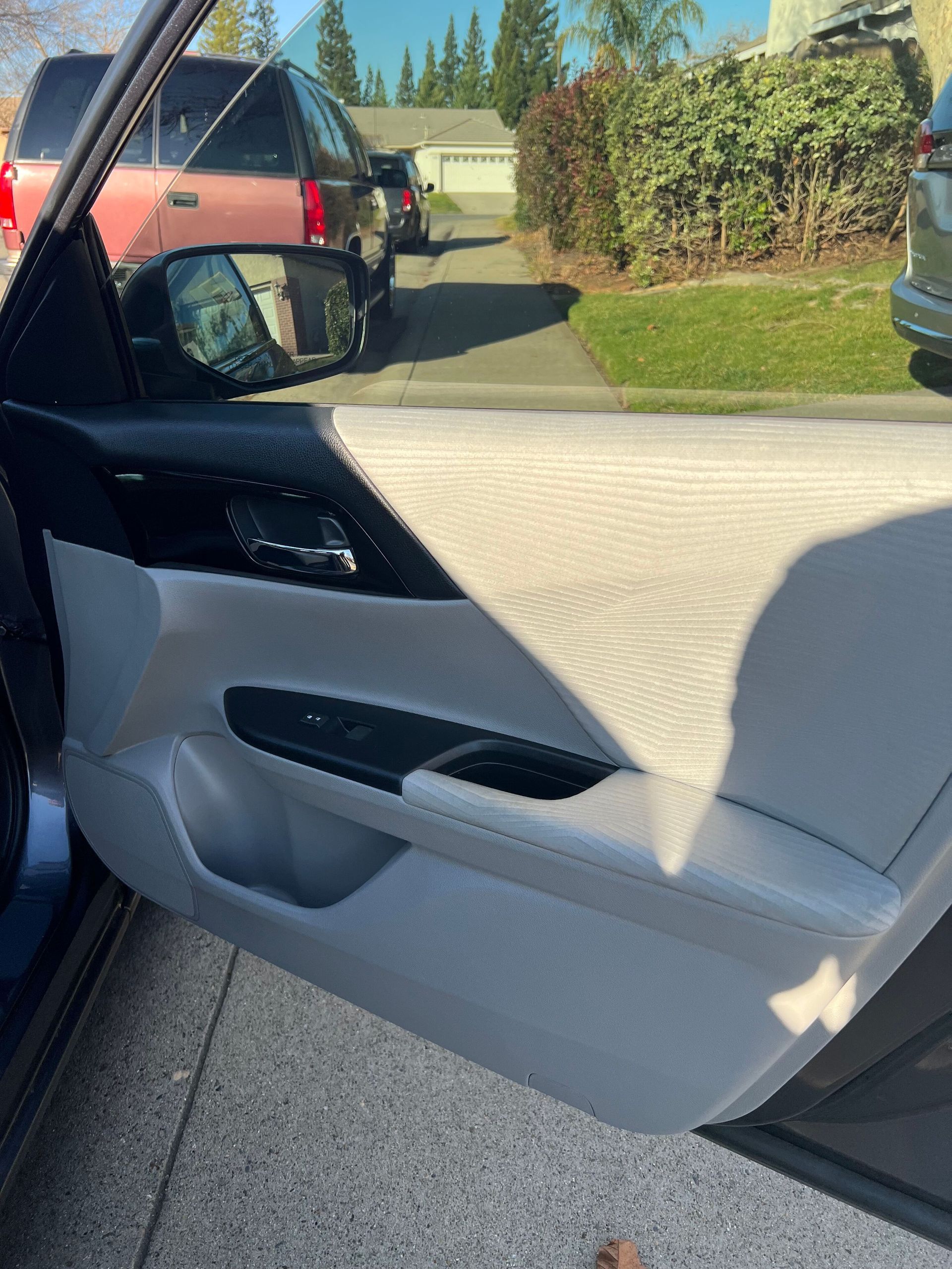 Car door interior with beige and black trim, open to a driveway and parked vehicles outside.