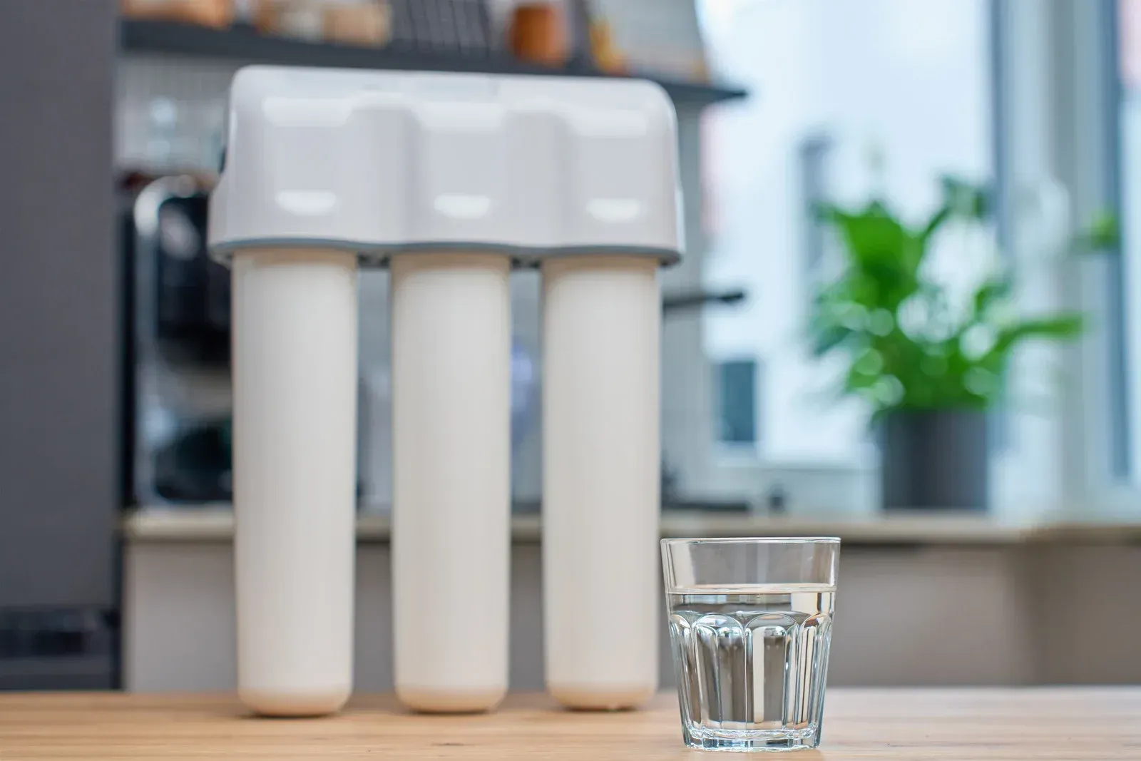 Water filter system with a glass of water on a wooden surface, blurred background.