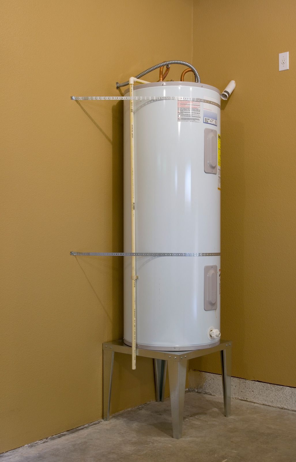 White water heater in a tan utility room with metal support brackets and exposed pipes