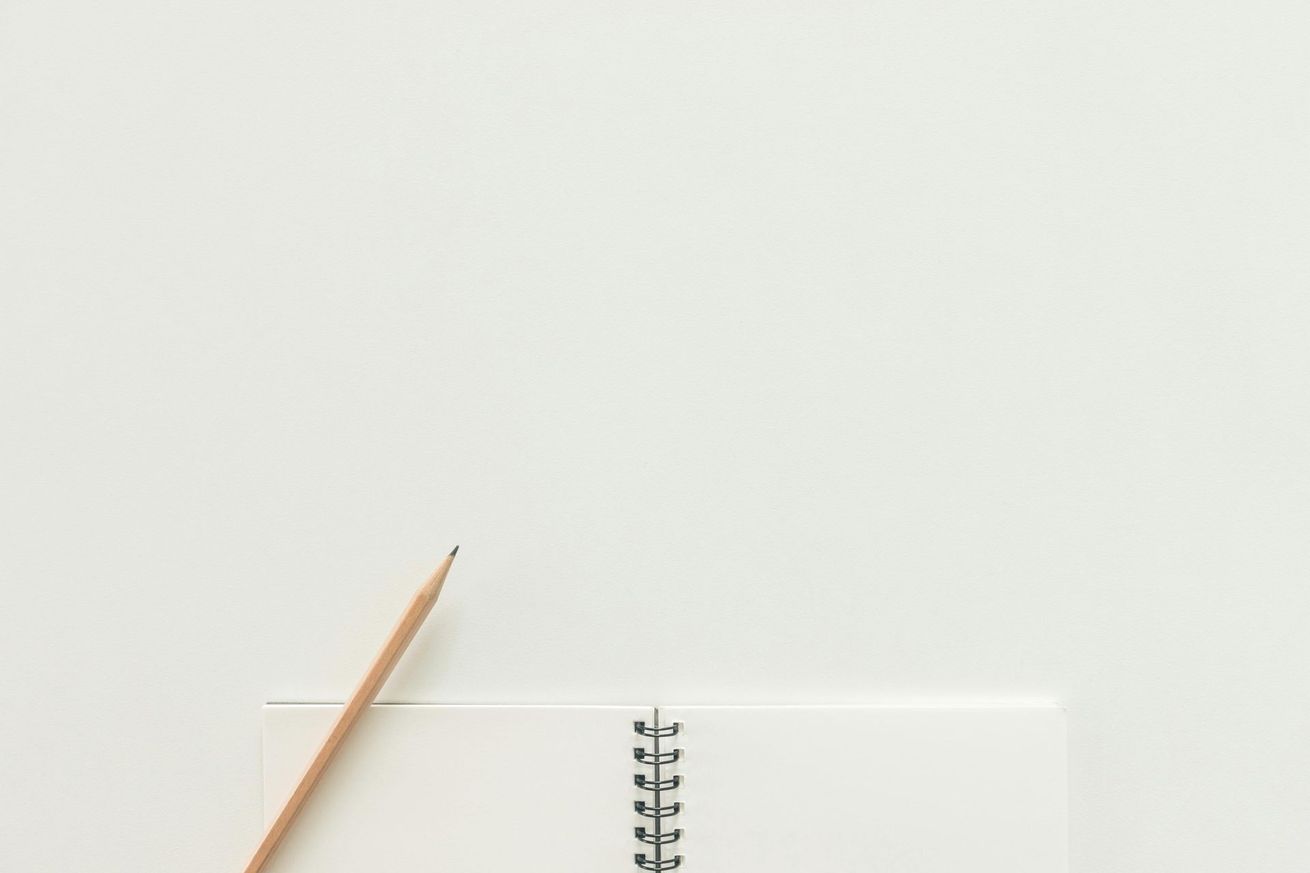A pencil is sitting on top of a spiral notebook on a white table.