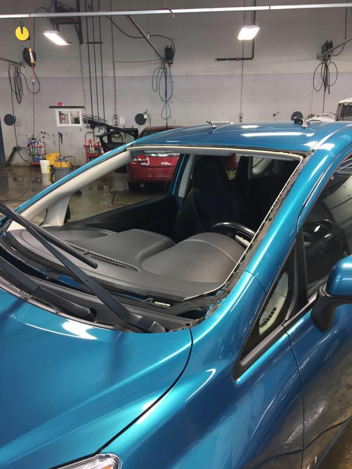 A blue car with a broken windshield is parked in a garage.