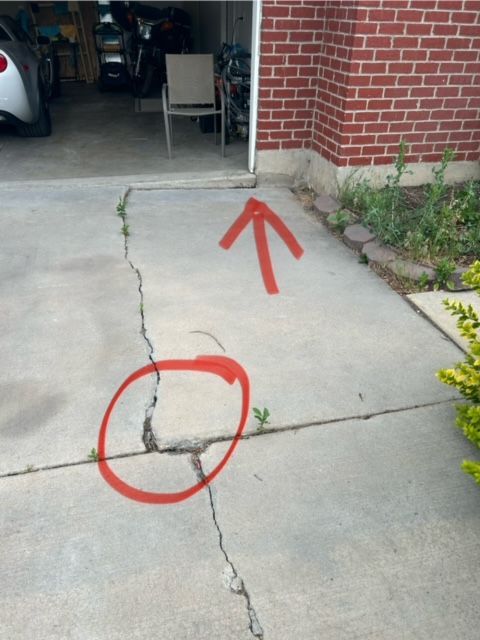 A cracked concrete driveway with a red arrow pointing up