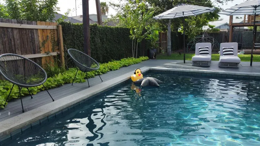 Person in a yellow float in a backyard swimming pool with lounge chairs and an umbrella nearby