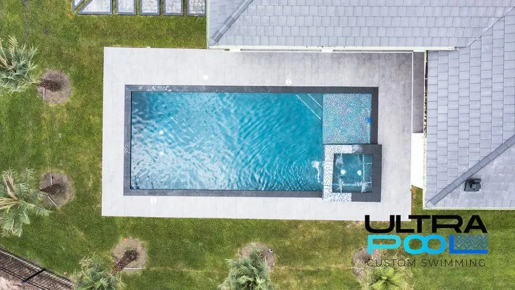 Top-down view of a rectangular backyard pool with blue water and surrounding patio and grass