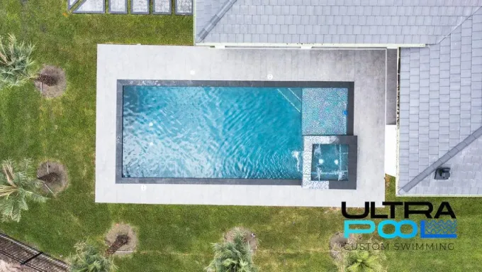 Top-down view of a rectangular swimming pool with blue water and a surrounding patio and lawn