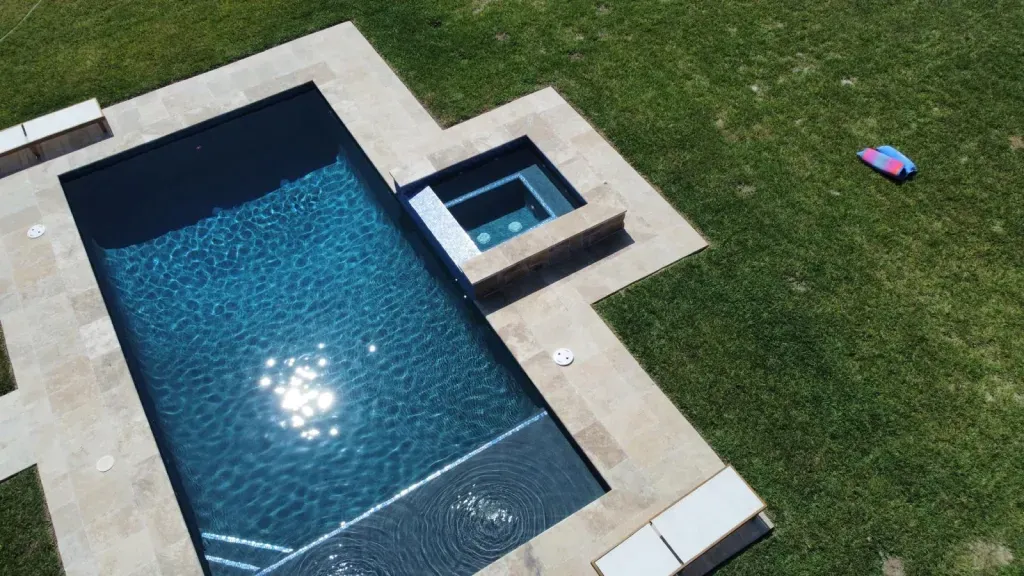Aerial view of a rectangular in-ground pool with a small hot tub beside it and green lawn nearby.
