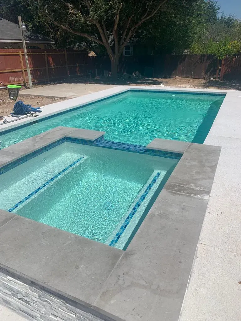 Backyard swimming pool with a shallow tanning ledge and gray concrete deck beside turquoise water