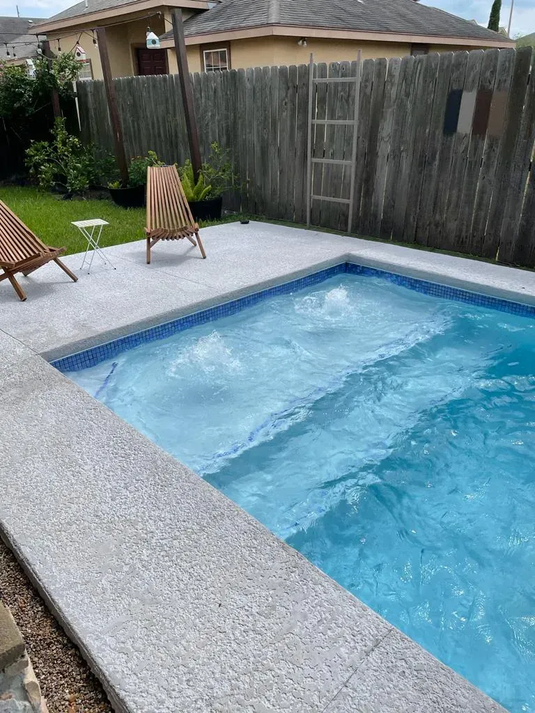 Small backyard swimming pool with two chairs on a concrete deck beside a wooden fence.