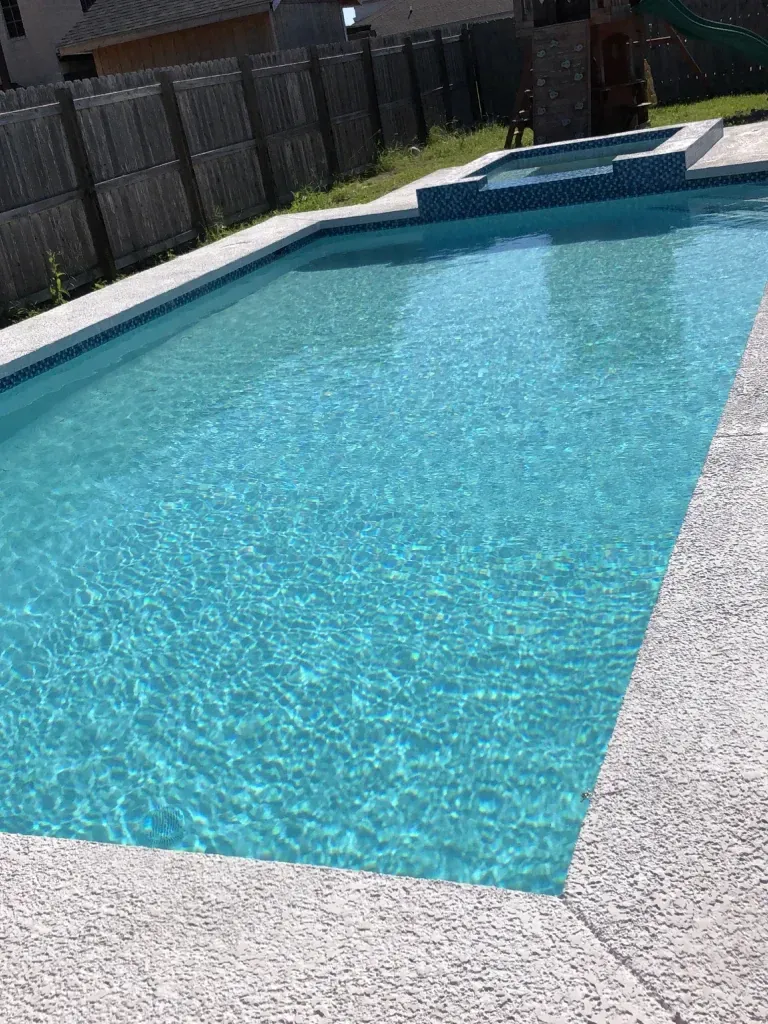 Rectangular backyard swimming pool with clear blue water and white stone decking