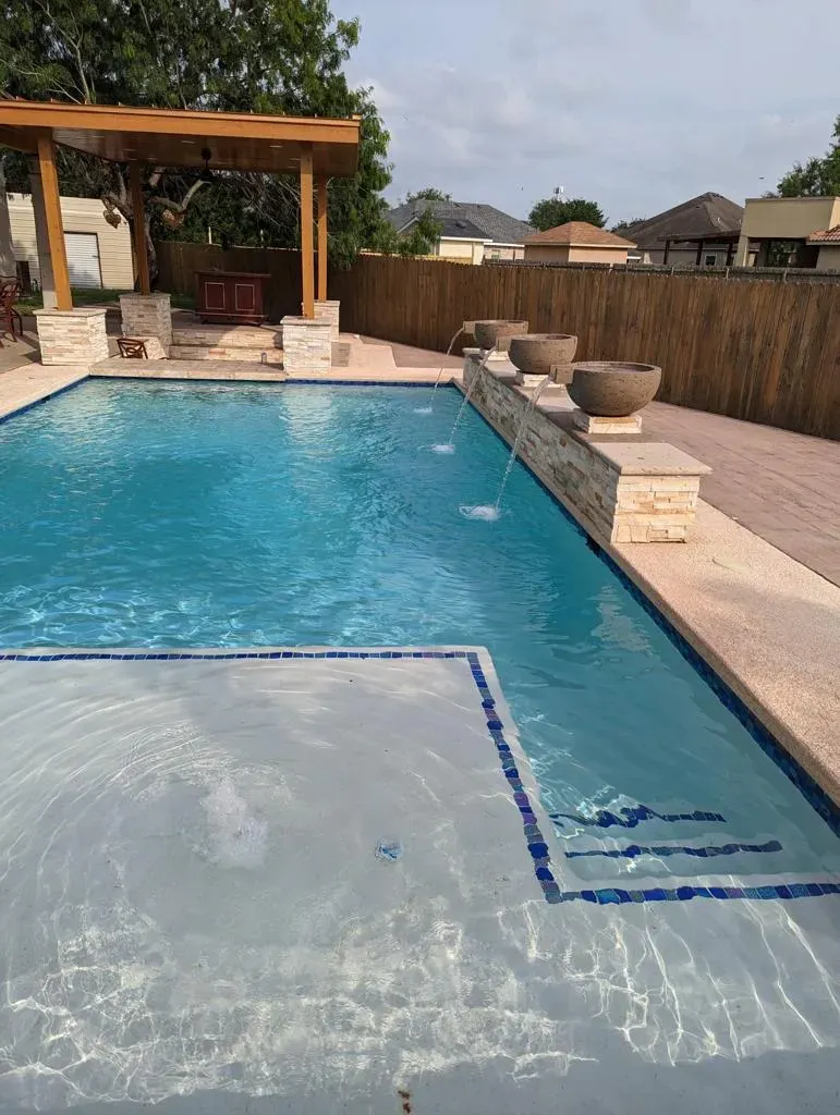 Backyard swimming pool with sun shelf, stone patio, and pergola seating area