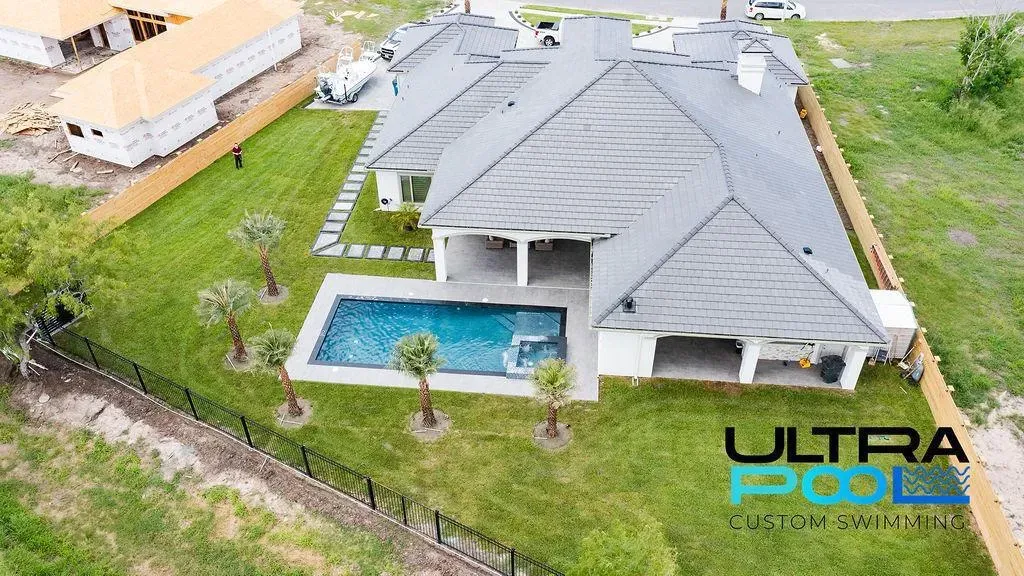 Aerial view of a modern house with a backyard pool and green lawn, featuring a gray roof and patio.