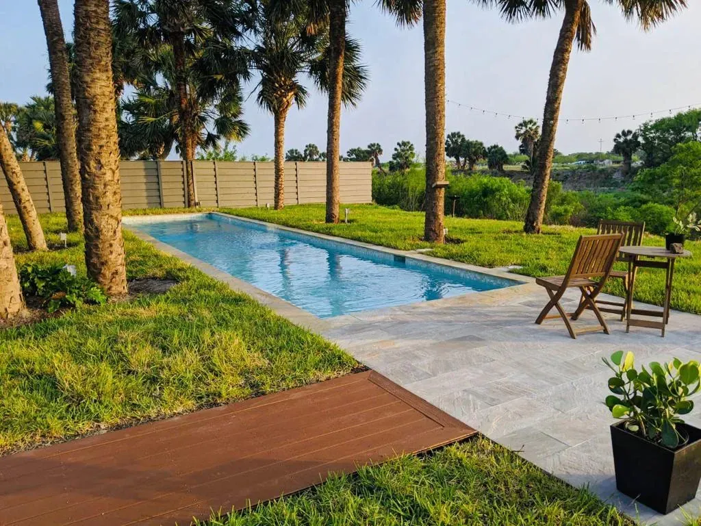 Backyard pool with palm trees, lawn, deck chairs, and a wooden walkway