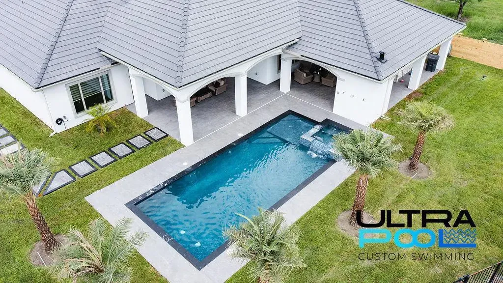 Aerial view of a modern white house with a rectangular blue swimming pool and patio.