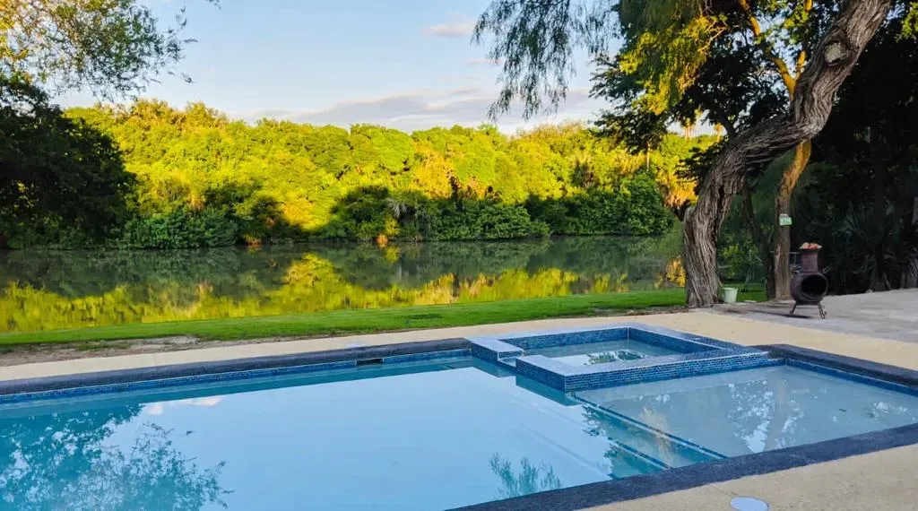Swimming pool beside a lush green landscape at sunset, with a person standing near a tree.