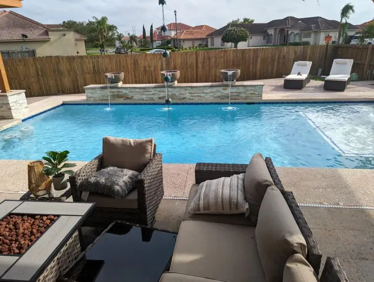 Backyard pool with lounge chairs, wicker seating, and a wooden fence in the background