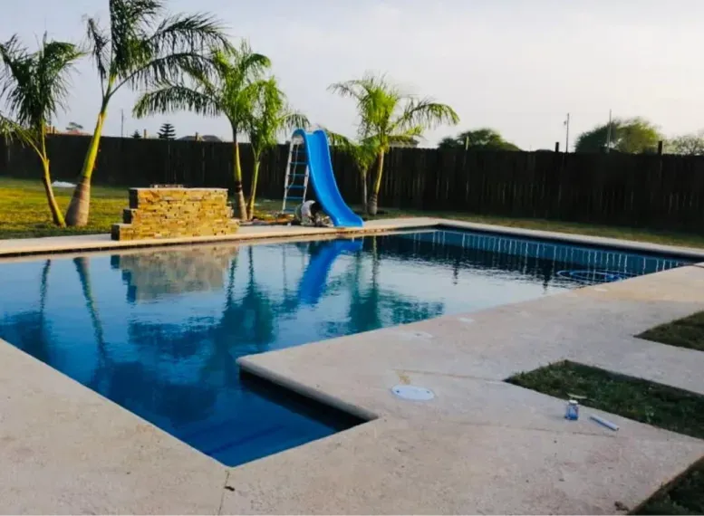 Backyard swimming pool with blue water, a slide, palm trees, and a stone deck