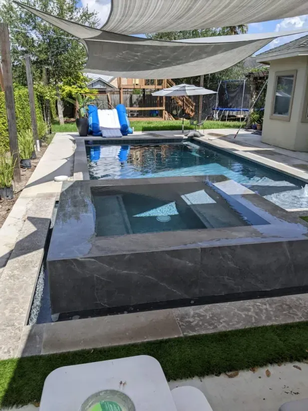 Modern backyard pool with shaded lounge chairs, clear water, and a raised spa area