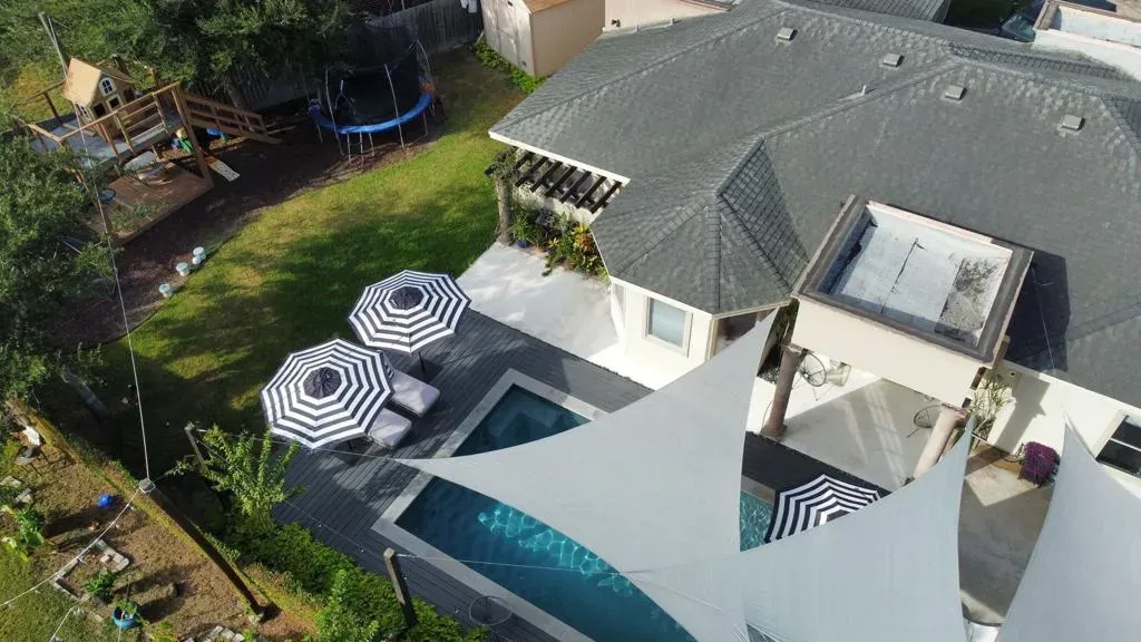 Aerial view of a backyard patio with black-and-white umbrellas, lounge chairs, lawn, and a gray-roofed house.