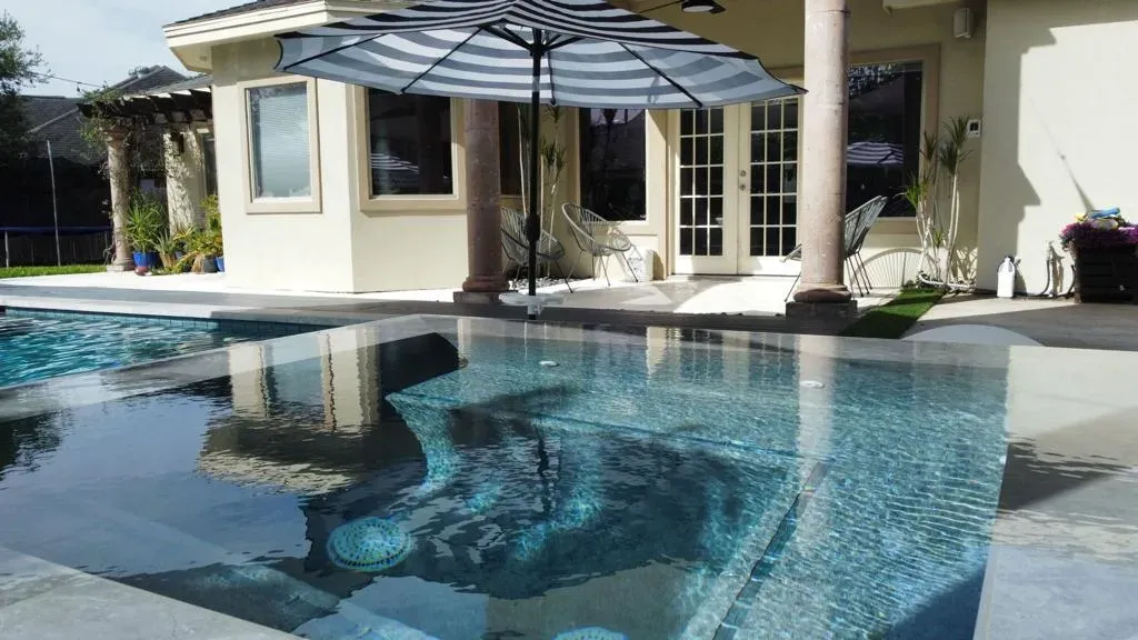 Backyard swimming pool with clear blue water, patio umbrella, and house reflecting in the water