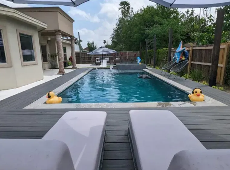 Backyard pool with two lounge chairs in the foreground and rubber ducks floating in the water.