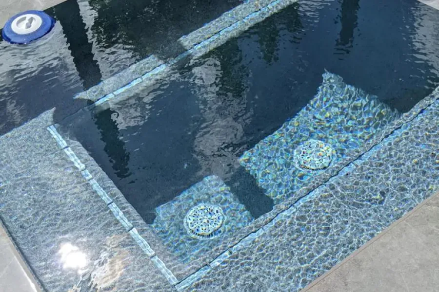 Blue-tiled swimming pool with clear water, steps, and round pool lights near the edge