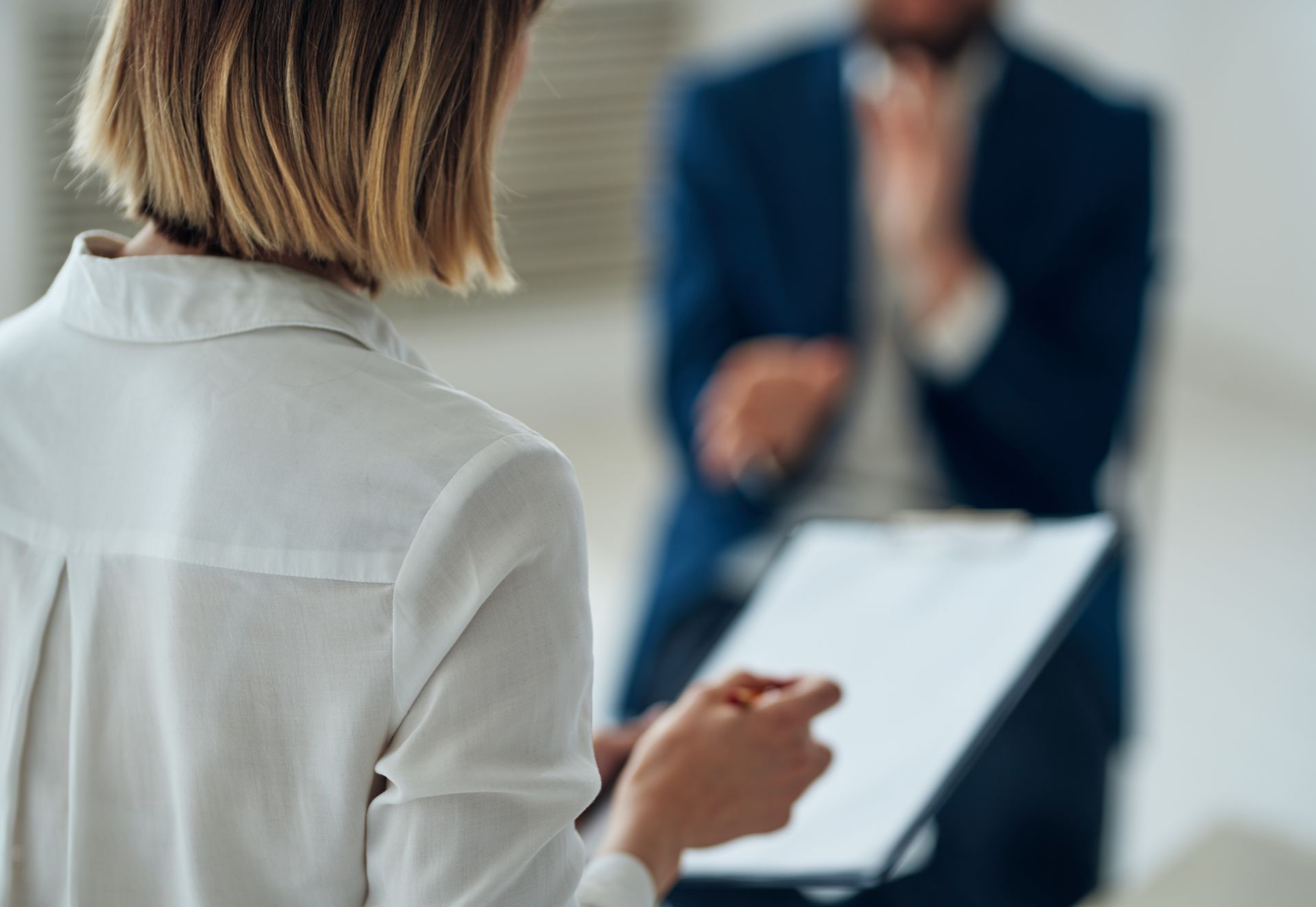 Person taking notes during an interview with a blurred speaker in the background