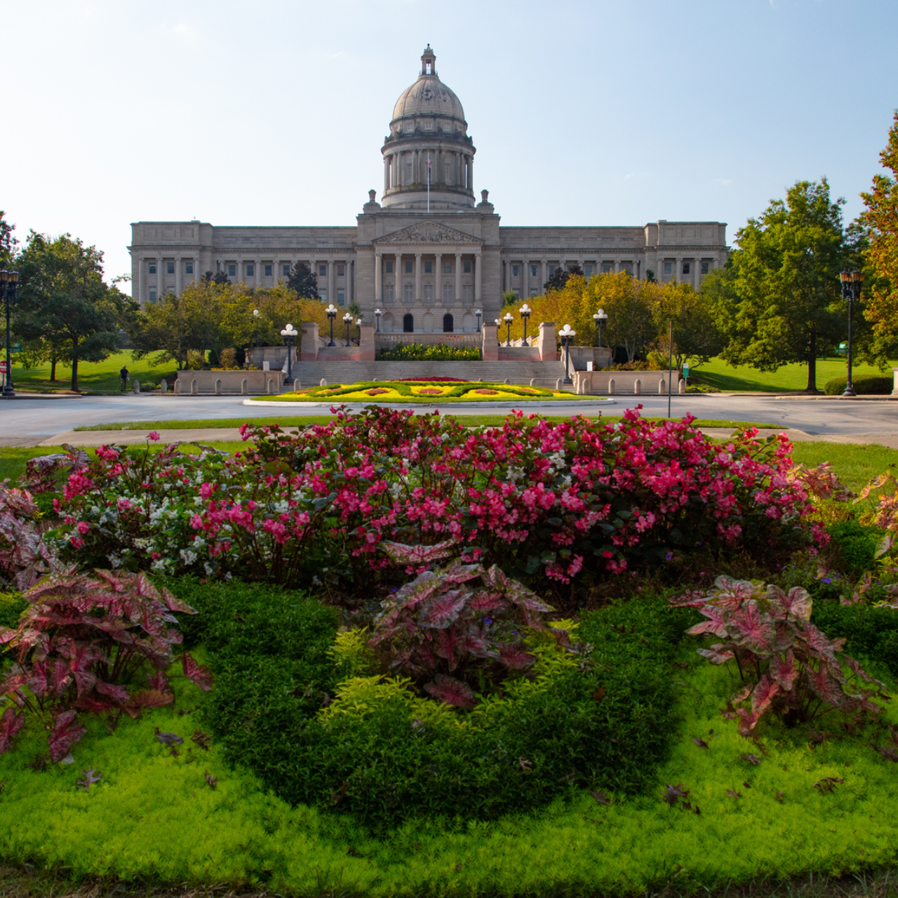 State capitol building behind a colorful flower garden and green lawn on a sunny day