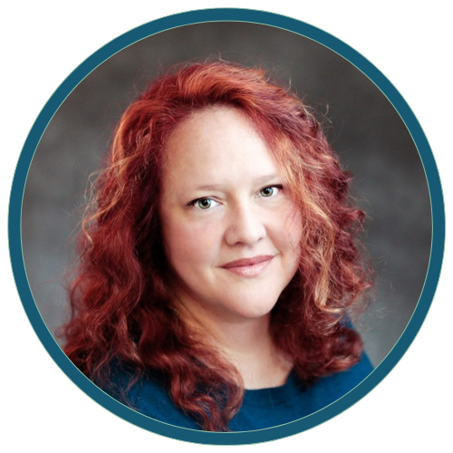 Studio headshot of a smiling red-haired woman in a teal top against a gray background