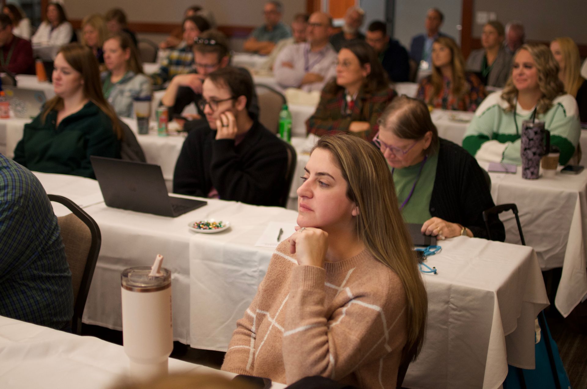 Conference audience seated at tables, listening and taking notes in a meeting room