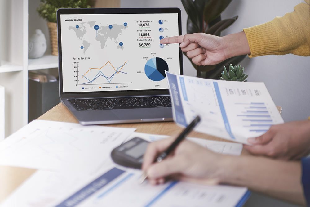 Two people analyzing financial data on a laptop and paper.