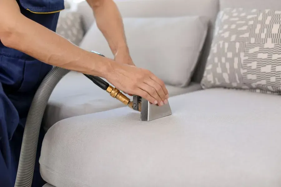 Person in Blue Uniform Cleaning a Light-coloured Sofa — Phil Lindfield's Big Red Carpet Cleaning In Taree, NSW