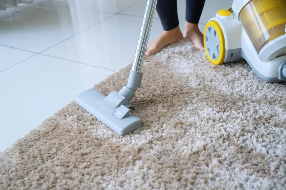 Vacuum Cleaner Cleaning a Beige Shag Rug on a Tiled Floor — Phil Lindfield's Big Red Carpet Cleaning In Nabiac, NSW