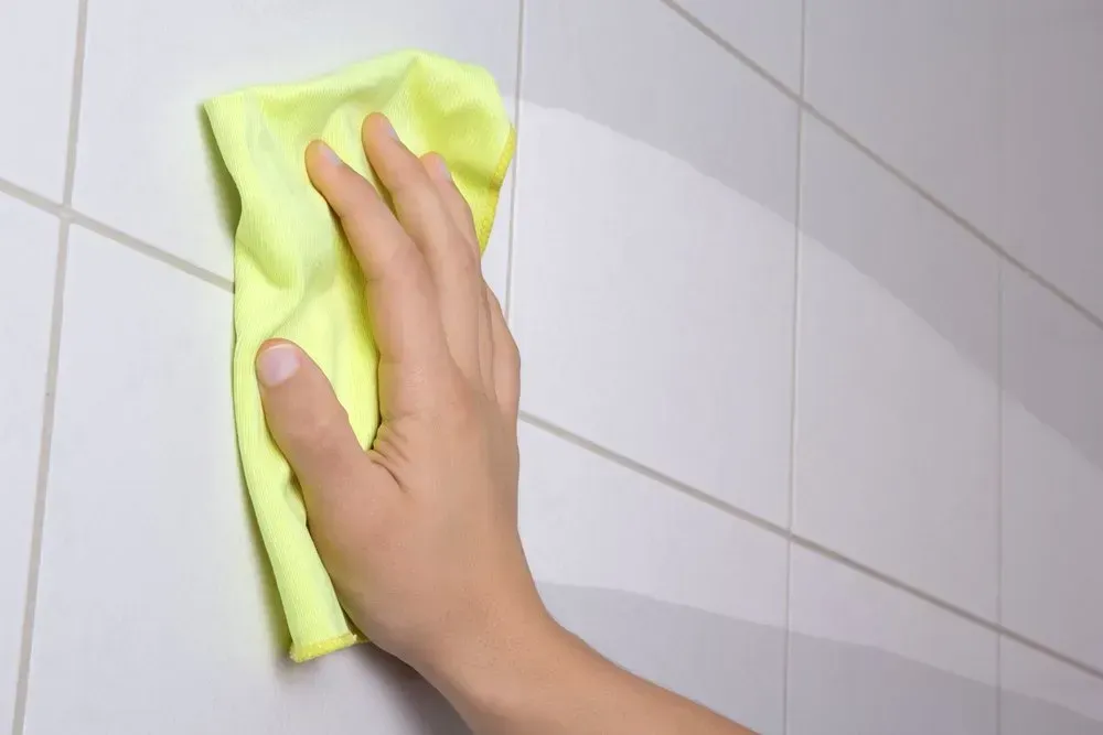 Hand Wiping a Yellow Cloth on White Tiled Wall — Phil Lindfield's Big Red Carpet Cleaning In Taree, NSW