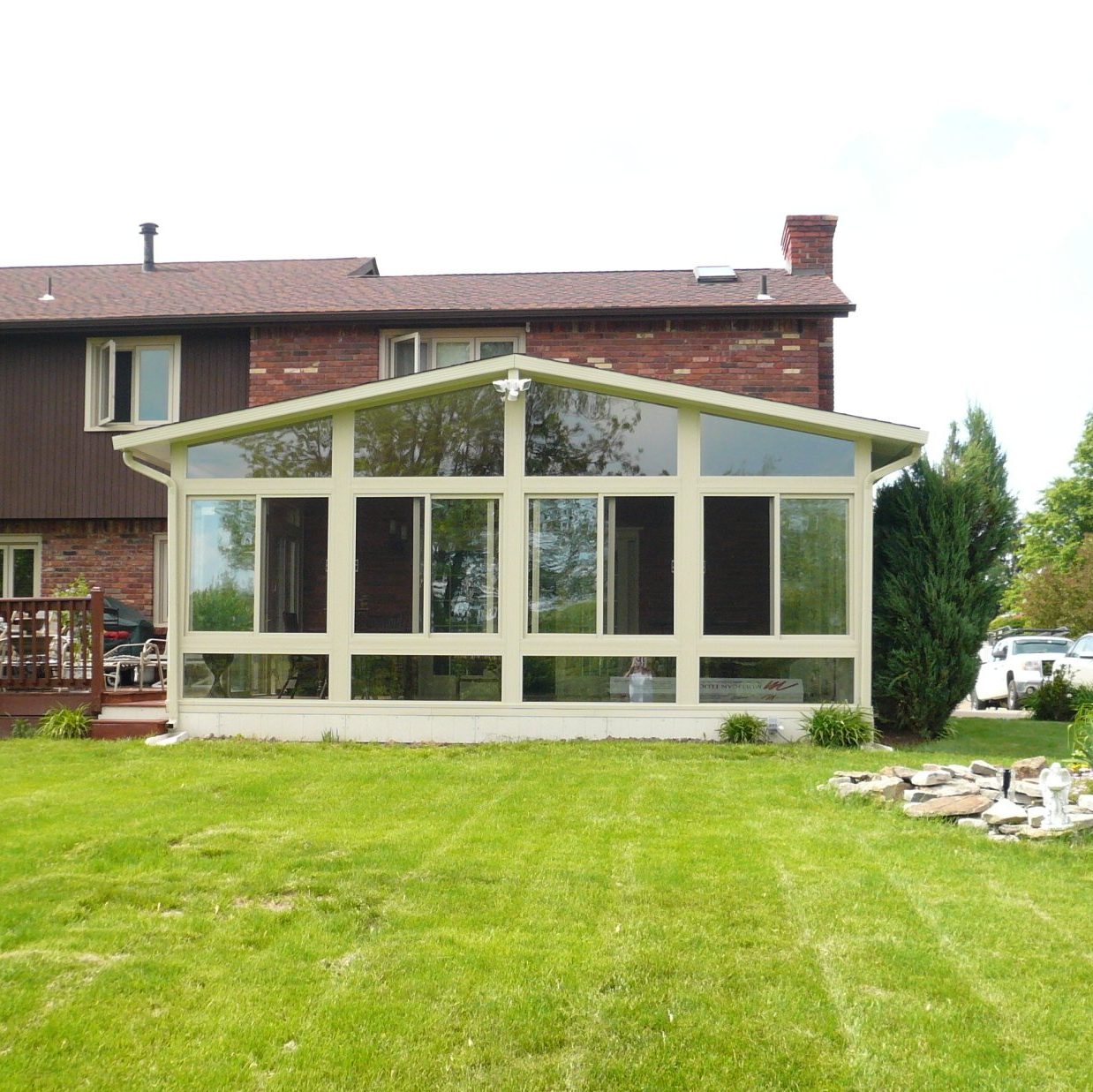 Sunroom addition with large windows on a brick home, set in a grassy backyard.