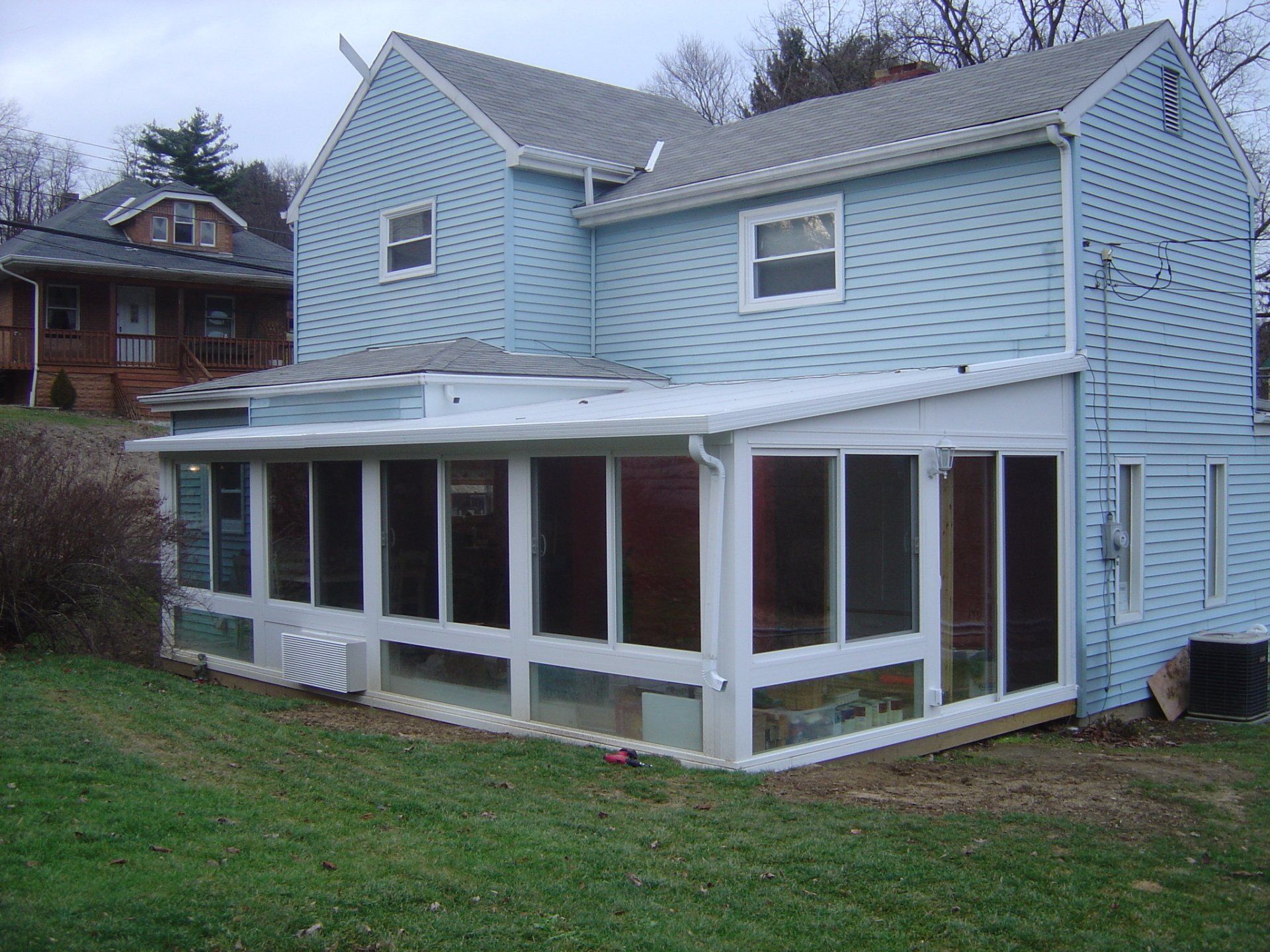 Blue two-story house with attached white sunroom on a green lawn, overcast day.