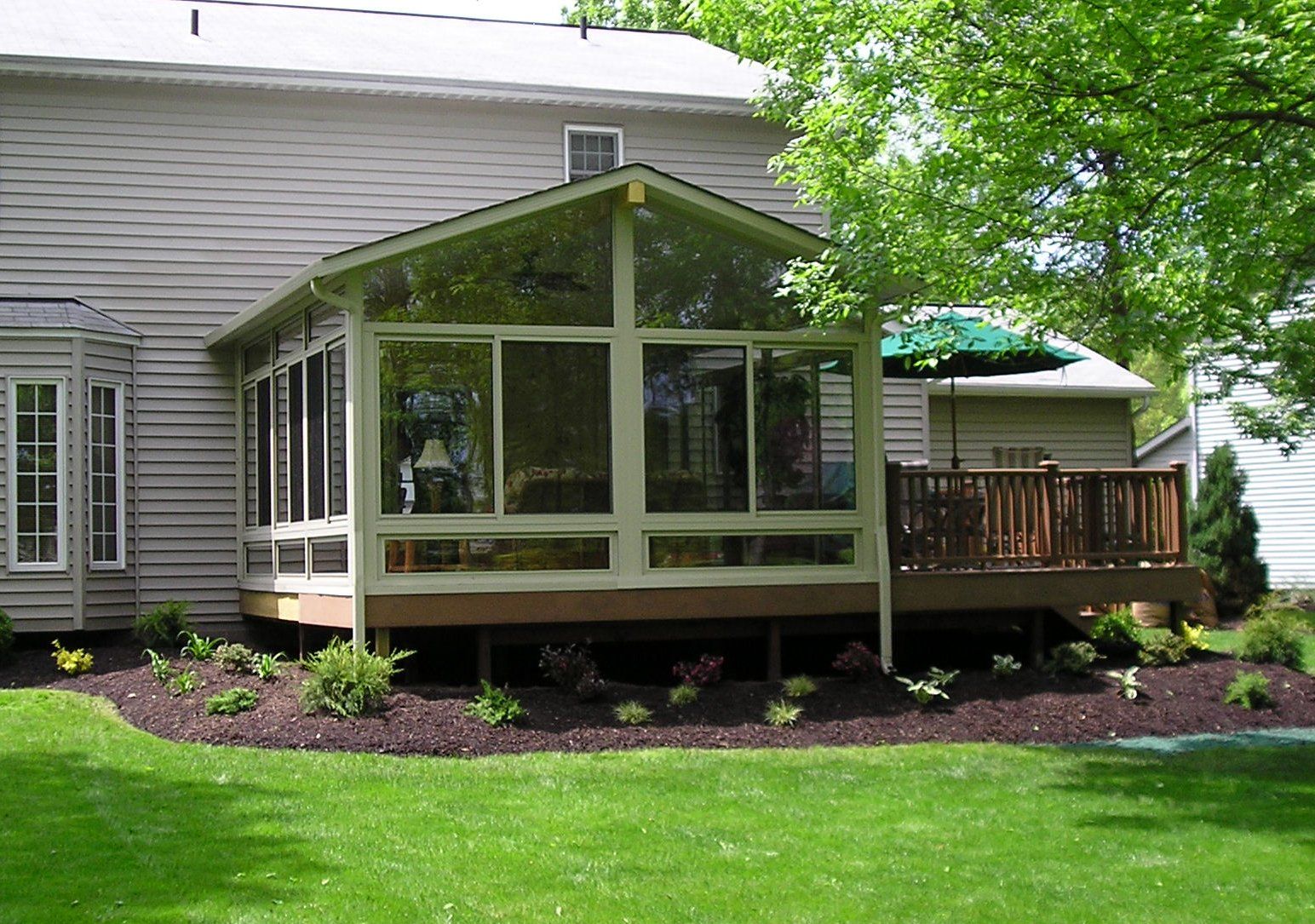 Screened-in porch attached to a house with a wooden deck and landscaped flower bed.