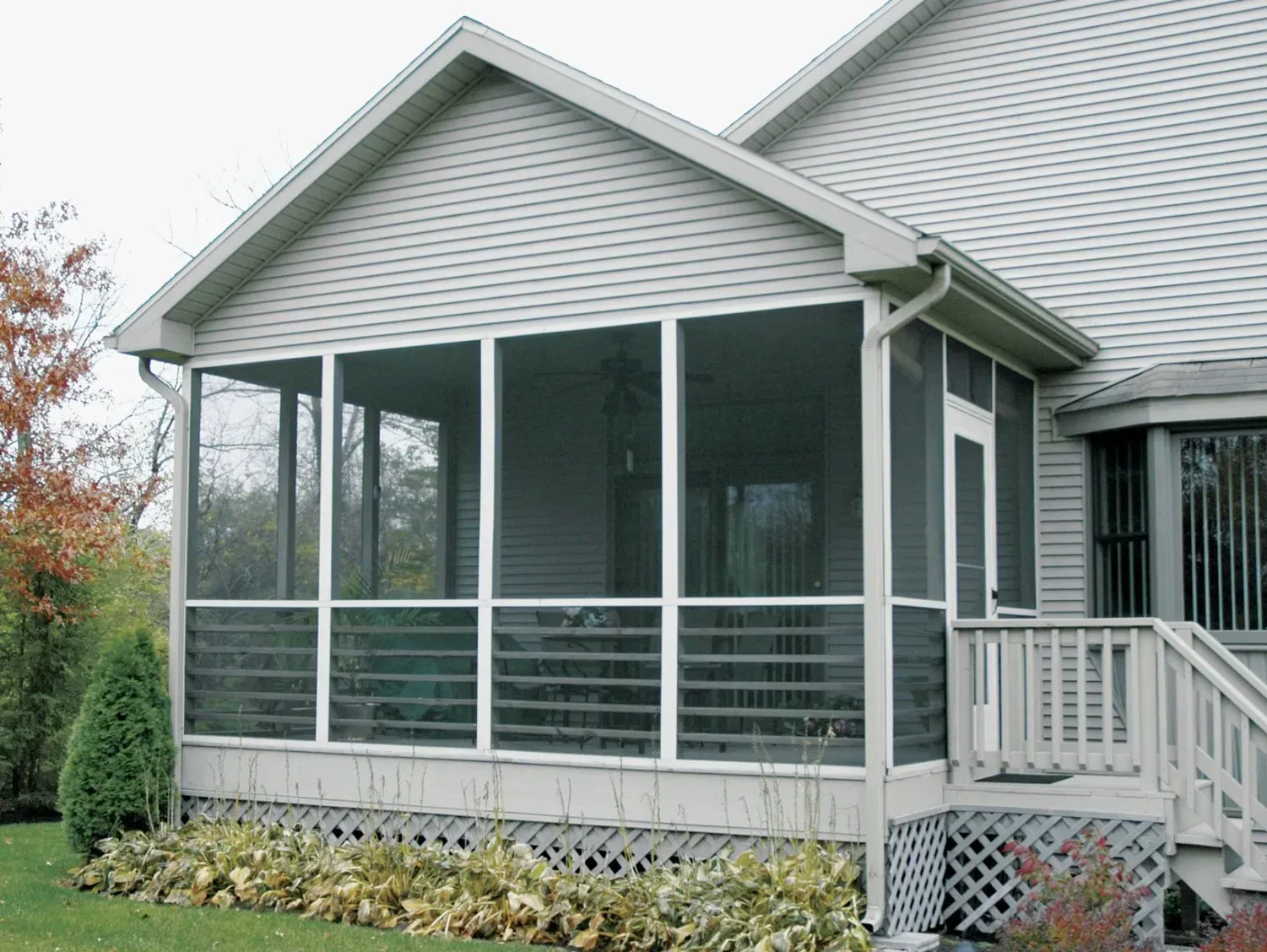 Screened-in porch attached to a light-colored house, featuring white frames and screens, with a visible door and railing.
