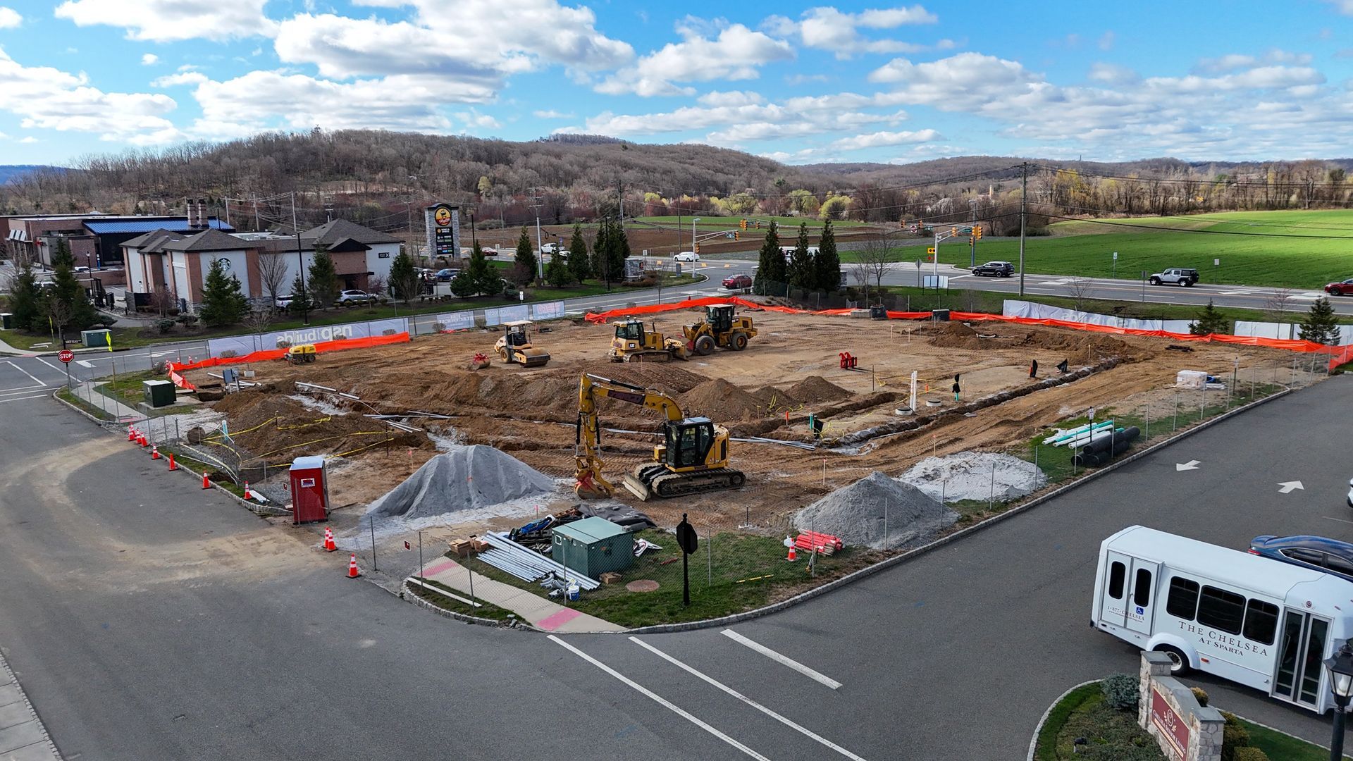 Construction site with excavators and foundation work in a fenced lot near roads and buildings