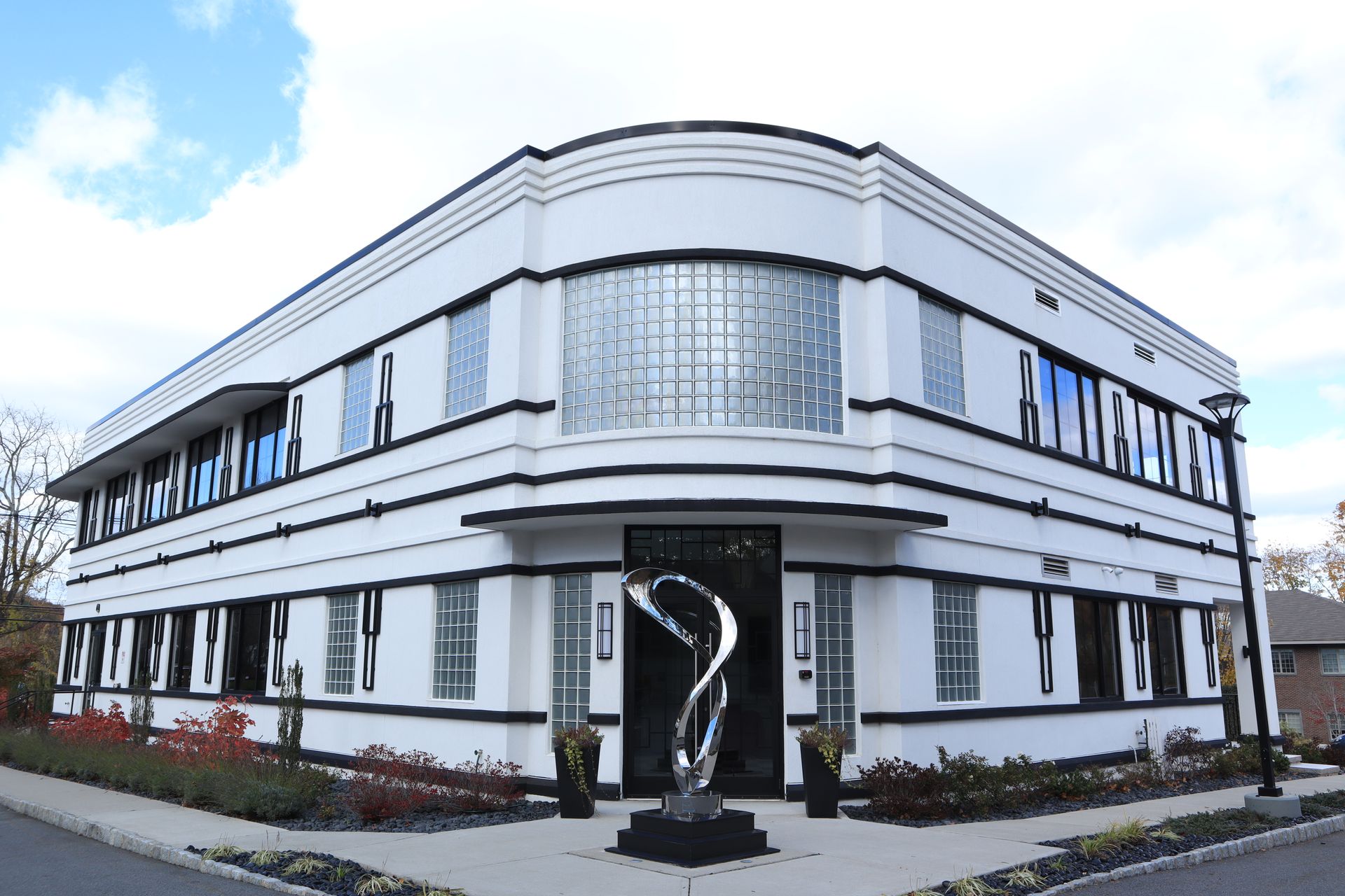 White art deco building with black trim, glass windows, and a sculpture in front.