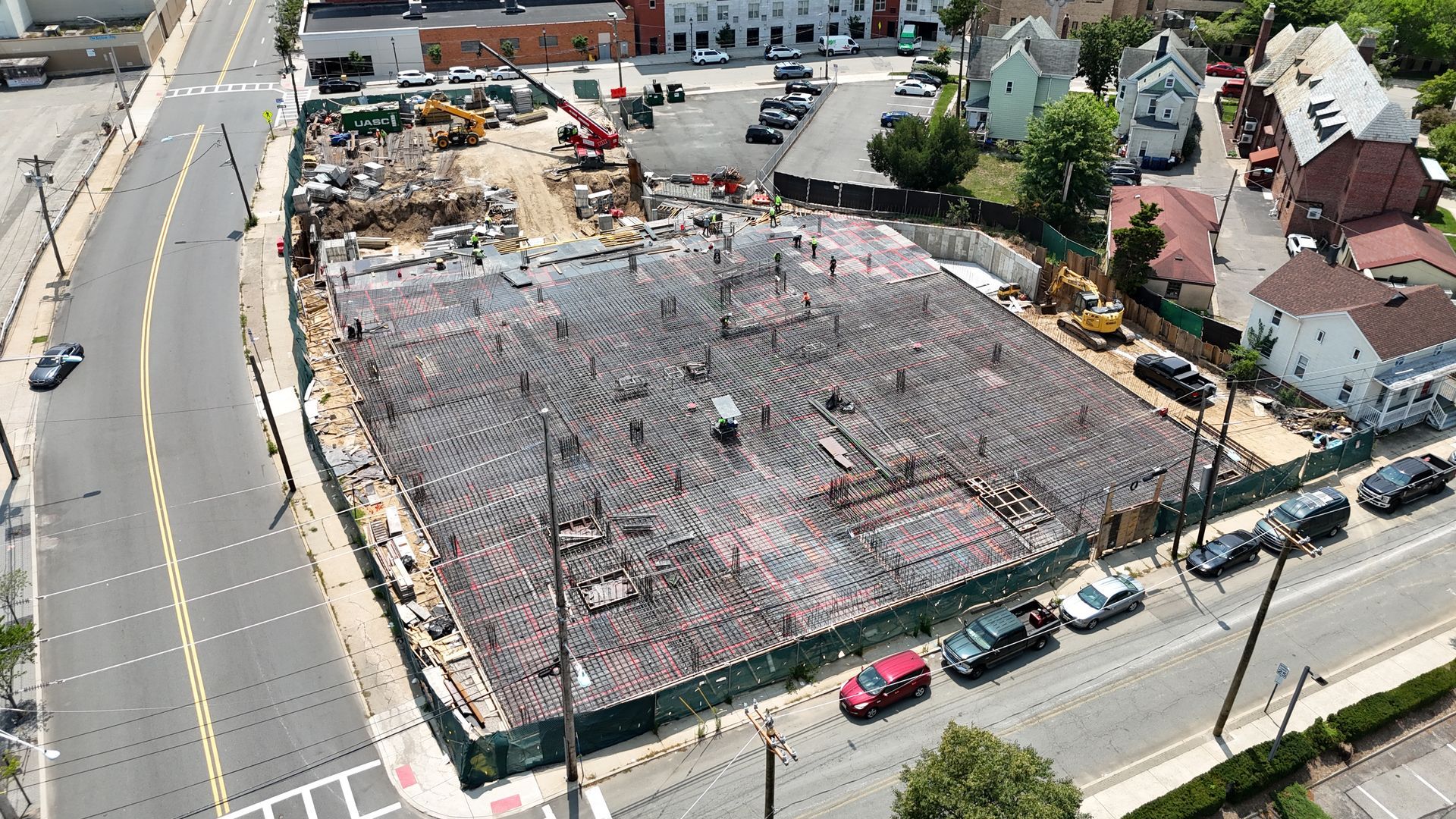 Aerial view of a demolition site with rubble, workers, and surrounding streets and houses.